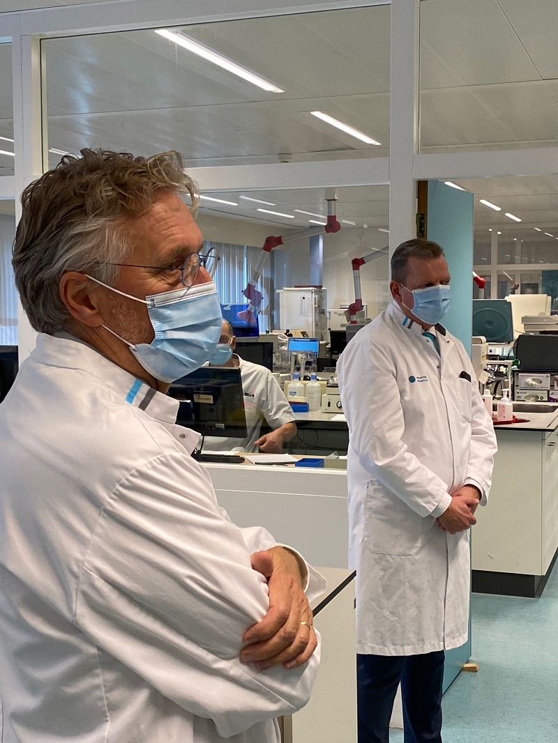 Twee mannen in witte jassen en mondkapjes staan in een lab bij het Catharina Ziekenhuis, met apparatuur en ramen achter zich.