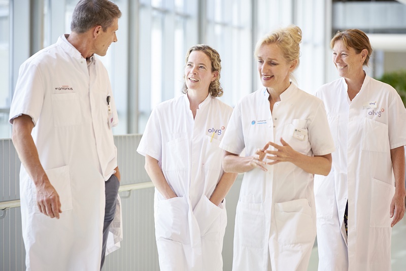 Vier medici van Santeon lopen in witte jassen lachend door een lichte bende met grote ramen, na winst van de VBHC Prize 2020.