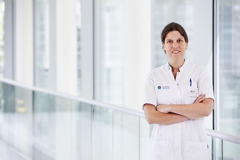 Internist-oncoloog Birgit Vriens met gekruiste armen in lichte bende met grote ramen, gericht op nazorg borstkankerpatiënten.