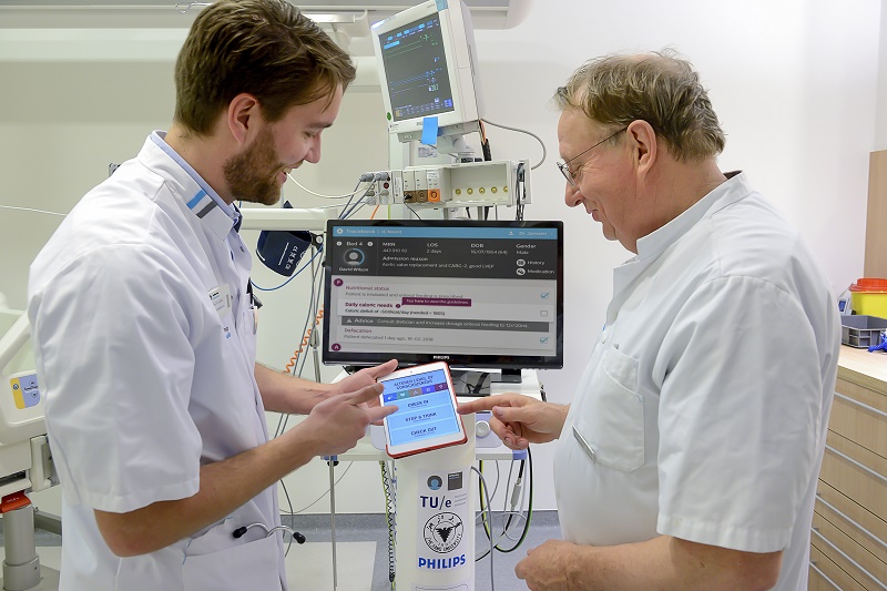 Twee mannelijke artsen in witte jassen bekijken op een tablet info met beslissingsondersteunend systeem in ziekenhuisruimte.