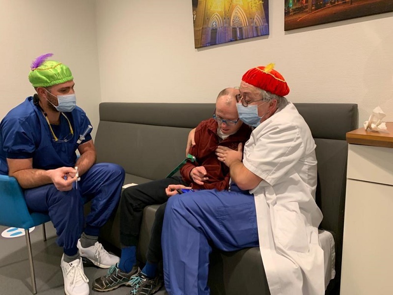 Drie volwassenen met mondmaskers en gekleurde hoeden in een ziekenhuiskamer, een toont een MRI en een speelgoedstoomboot.