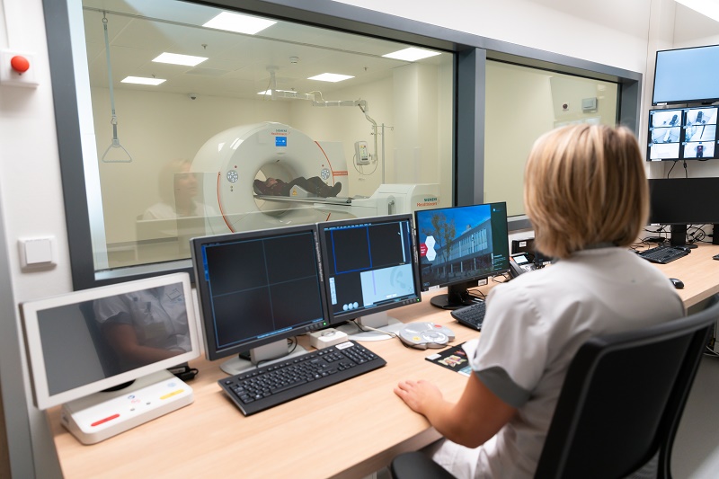 Een technicus in het Catharina Ziekenhuis volgt een PET-CT-scan op via computerschermen, gescheiden door een glazen staaf.