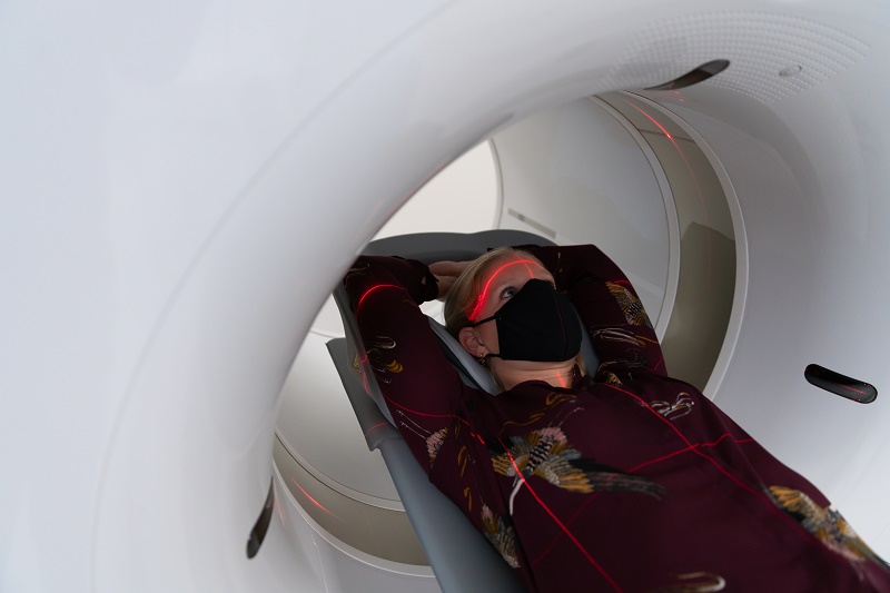 Een persoon met een mondkapje ligt op de rug, armen boven het hoofd, in een PET-CT-scanner in het Catharina Ziekenhuis.