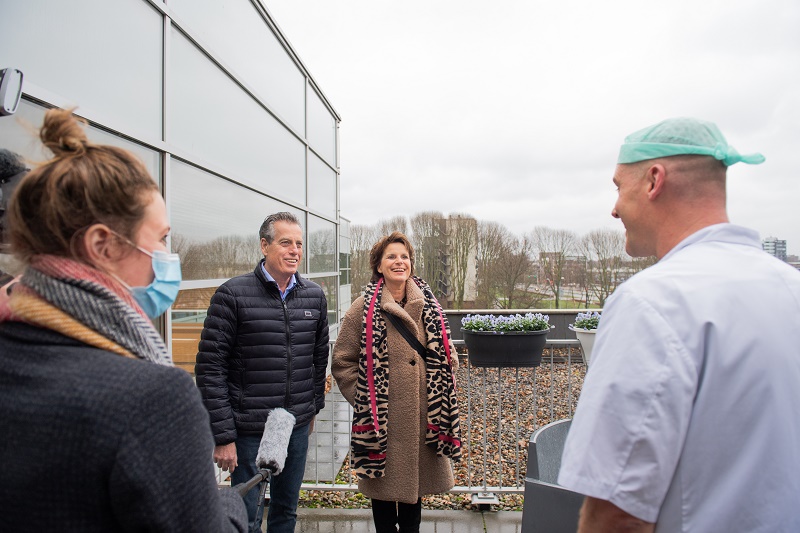 Vier volwassenen op een dakterras, waaronder een verpleegkundige en IC-patiënt. Planten en stadsgebouwen op de achtergrond.