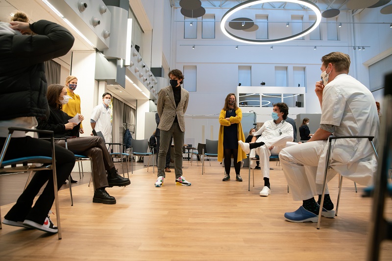 Groep mensen in moderne ruimte van Catharina Ziekenhuis; sommigen dragen mondkapjes en medische kleding, anderen casual of zakelijk.