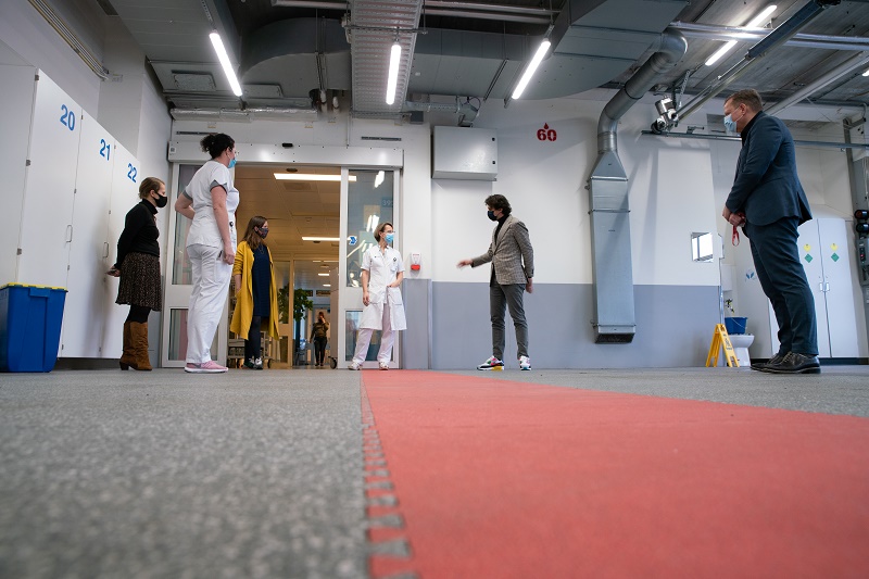 Mensen, waaronder medisch personeel, staan verspreid in het Catharina Ziekenhuis bij rood tapijt en genummerde deuren tijdens de vaccinatieweek.