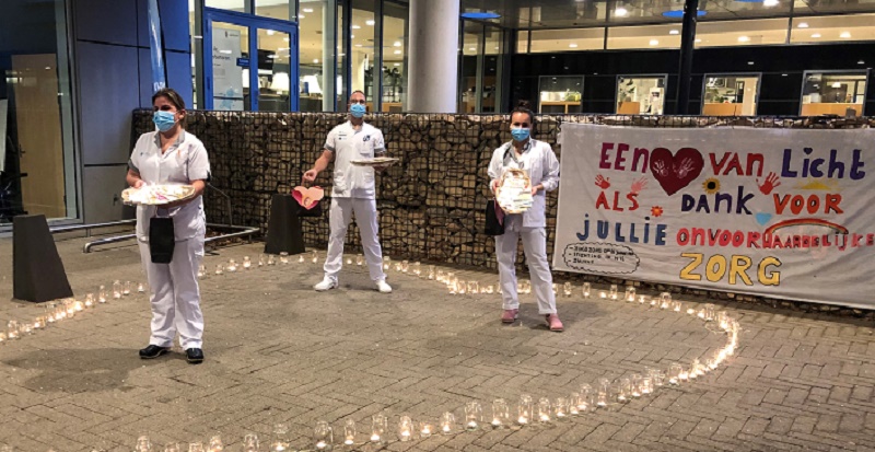 Drie zorgmedewerkers met mondkapjes staan in een hart van kaarsen bij het Catharina Ziekenhuis. Banner bedankt zorgpersoneel.
