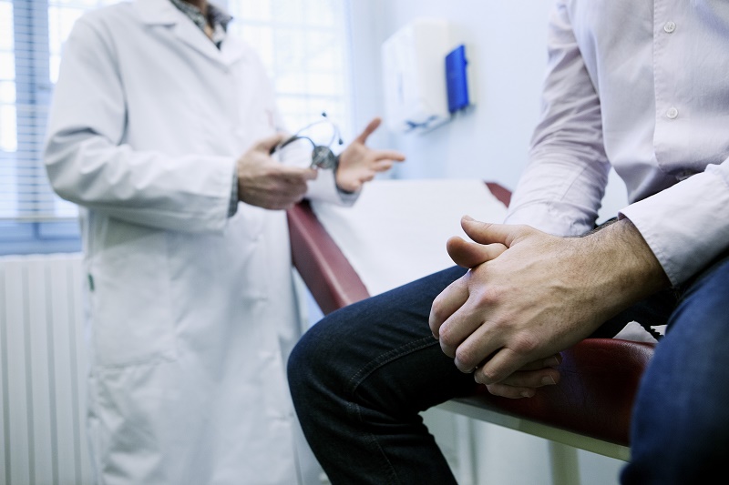 Een persoon zit op een onderzoekstafel, arts van Santeon ziekenhuizen bespreekt prostaatkankerdiagnostiek.