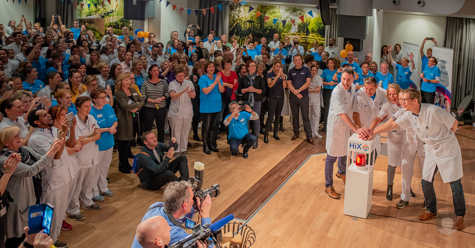 Groep mensen, veel in witte uniformen, binnen. Vier drukken op HiX-podiumknop bij de start van elektronisch patiëntendossier.