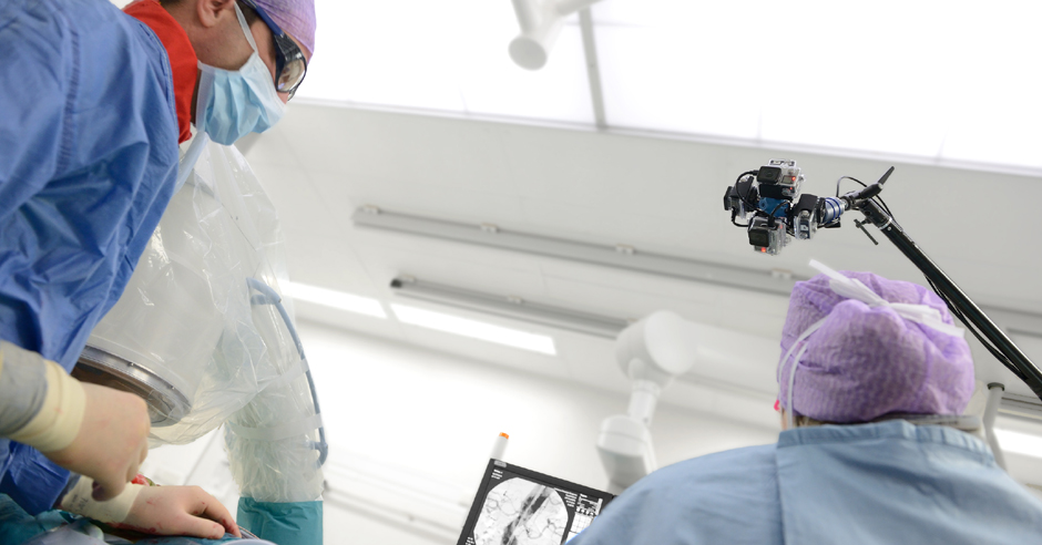 Twee medici in OK-kleding en mondmaskers kijken naar een scherm tijdens een vaatoperatie, terwijl een 360°-camera het filmt.