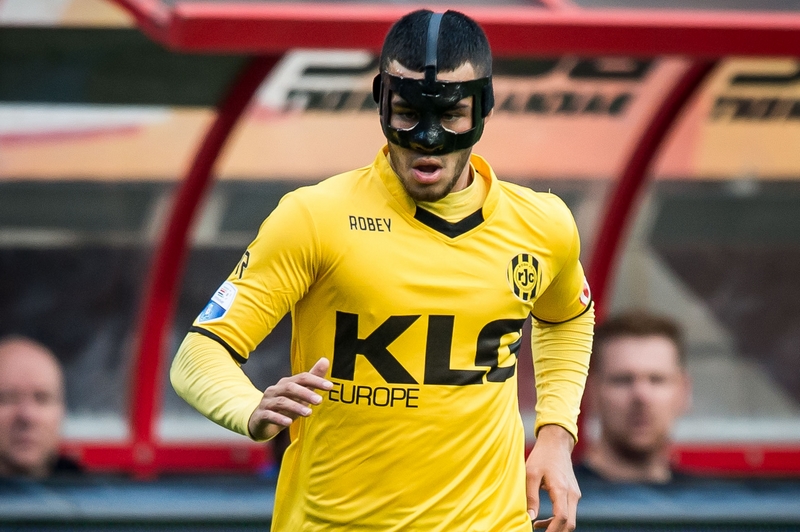 Een Roda JC-voetballer met geel shirt en zwart bestralingsmasker gehuurd op het veld; KLG Europe-logo op het shirt.