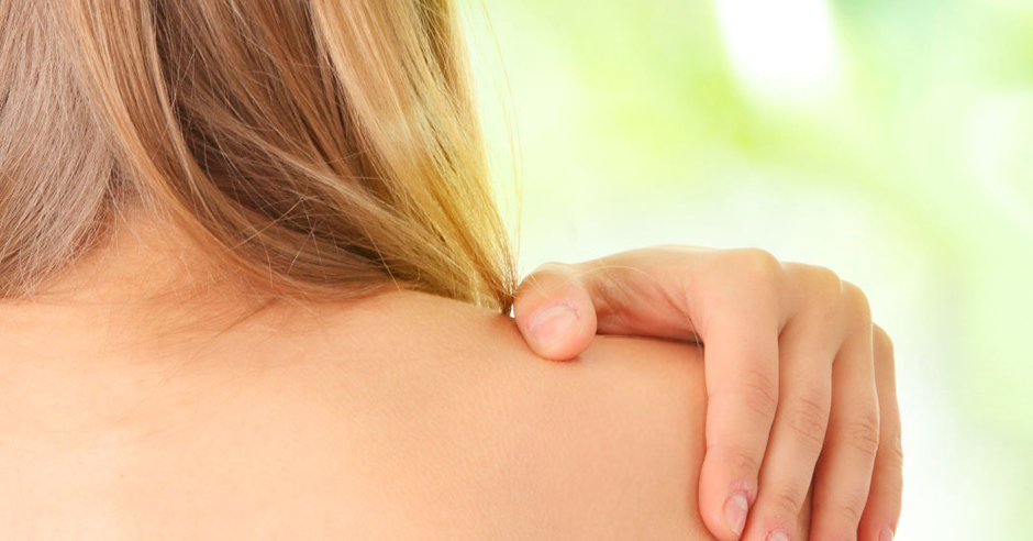 Persoon met lichte huid en blonde haar van achteren, hand op blote schouder, vage lichtgroene achtergrond.