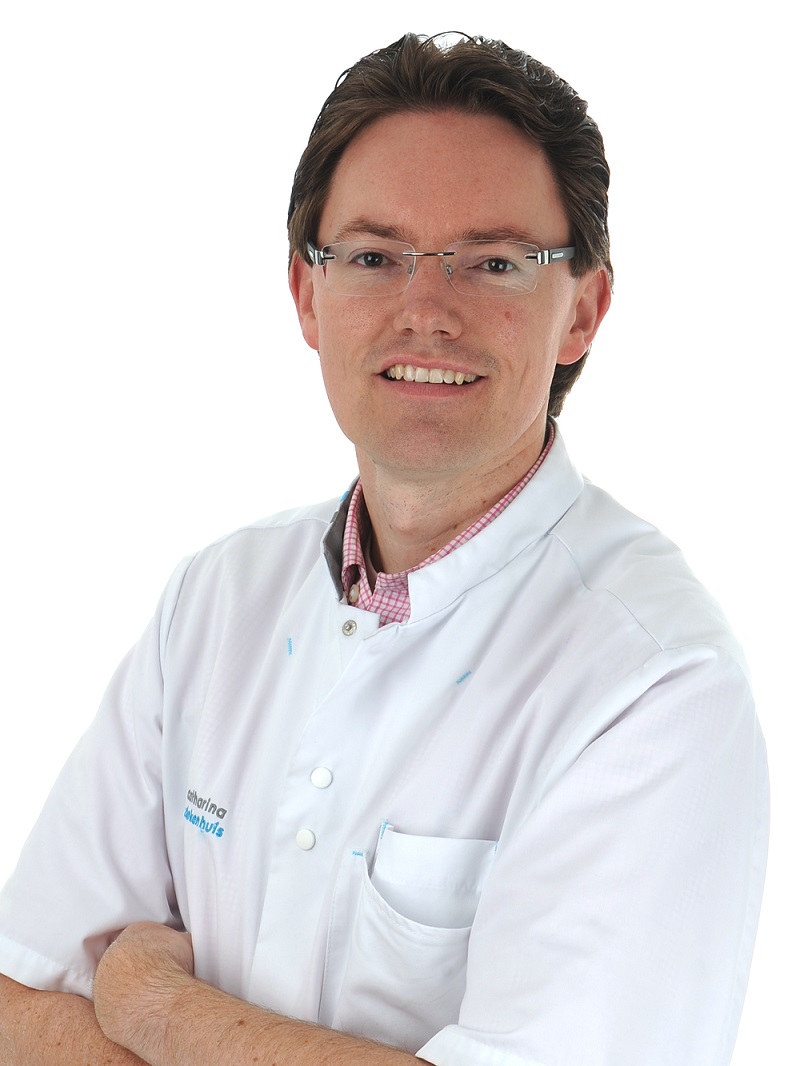 Persoon met bril en witte doktersjas staat met gekruiste armen en glimlacht, tegen witte achtergrond. Expert schildklierknobbels.