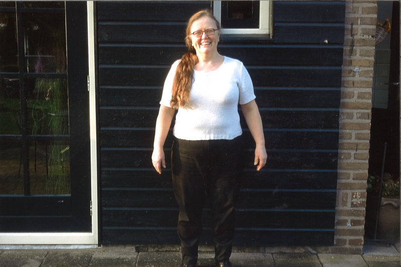 Lachende vrouw met lang roodbruin haar voor donkere houten toverstok. Joke van Stiphout draagt wit shirt en zwarte broek.