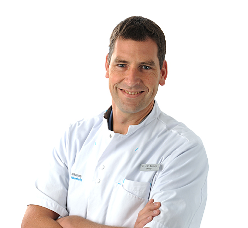 Een man in een witte doktersjas staat met gekruiste armen en glimlacht naar de camera tegen een witte achtergrond.