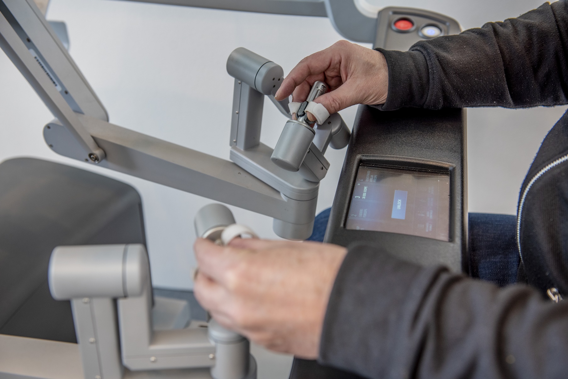 Iemand bestuurt een robotsysteem met twee grijze hendels en bekijkt behandelopties op een touchscreen display.