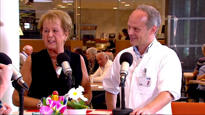 Oudere vrouwen en mannen in witte jas spreken met microfoons over leven met kanker; Annie van de Westerlo is een van de sprekers.