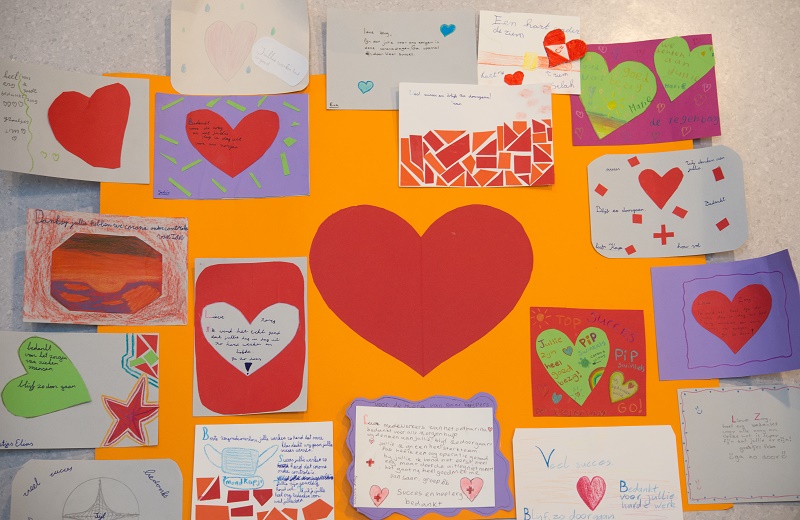 Oranje prikbord op basisschool De Regenboog met groot rood hart, omringd door kaarten, tekeningen en stickers vol steunbetuigingen.