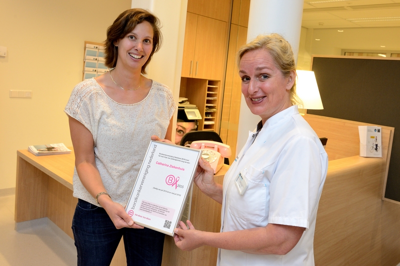 Twee vrouwen in het Catharina Ziekenhuis; een huisarts overhandigt een certificaat aan een lachende vrouw voor goede borstkankerzorg.