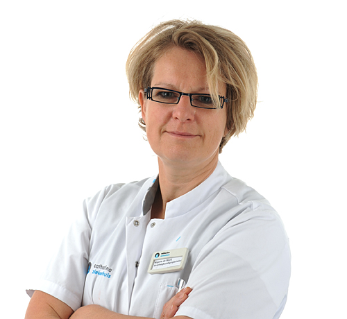 Persoon met kort blond haar en bril in witte doktersjas met naamkaartje, armen over elkaar, voor een witte achtergrond.