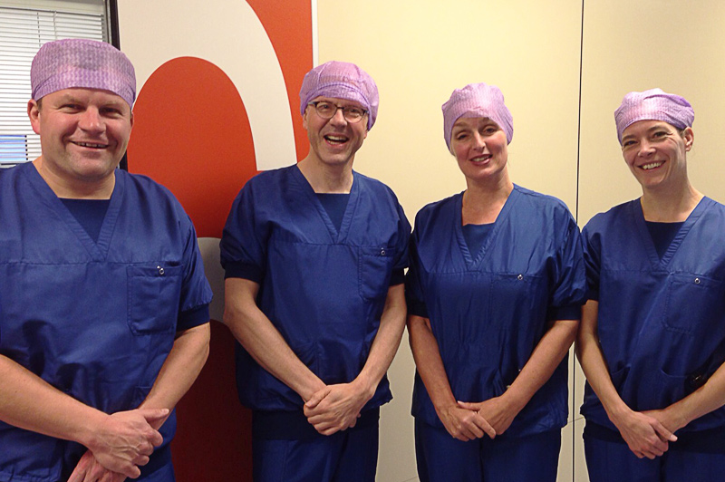 Vier mensen in blauwe scrubs en paarse haarnetjes staan binnen bij Mammacentrum Catharina Ziekenhuis voor een crèmekleurige muur.