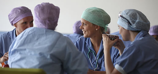 Vier medisch professionals in scrubs en mutsen praten samen in het Catharina Ziekenhuis. Eén persoon houdt een beker vast.
