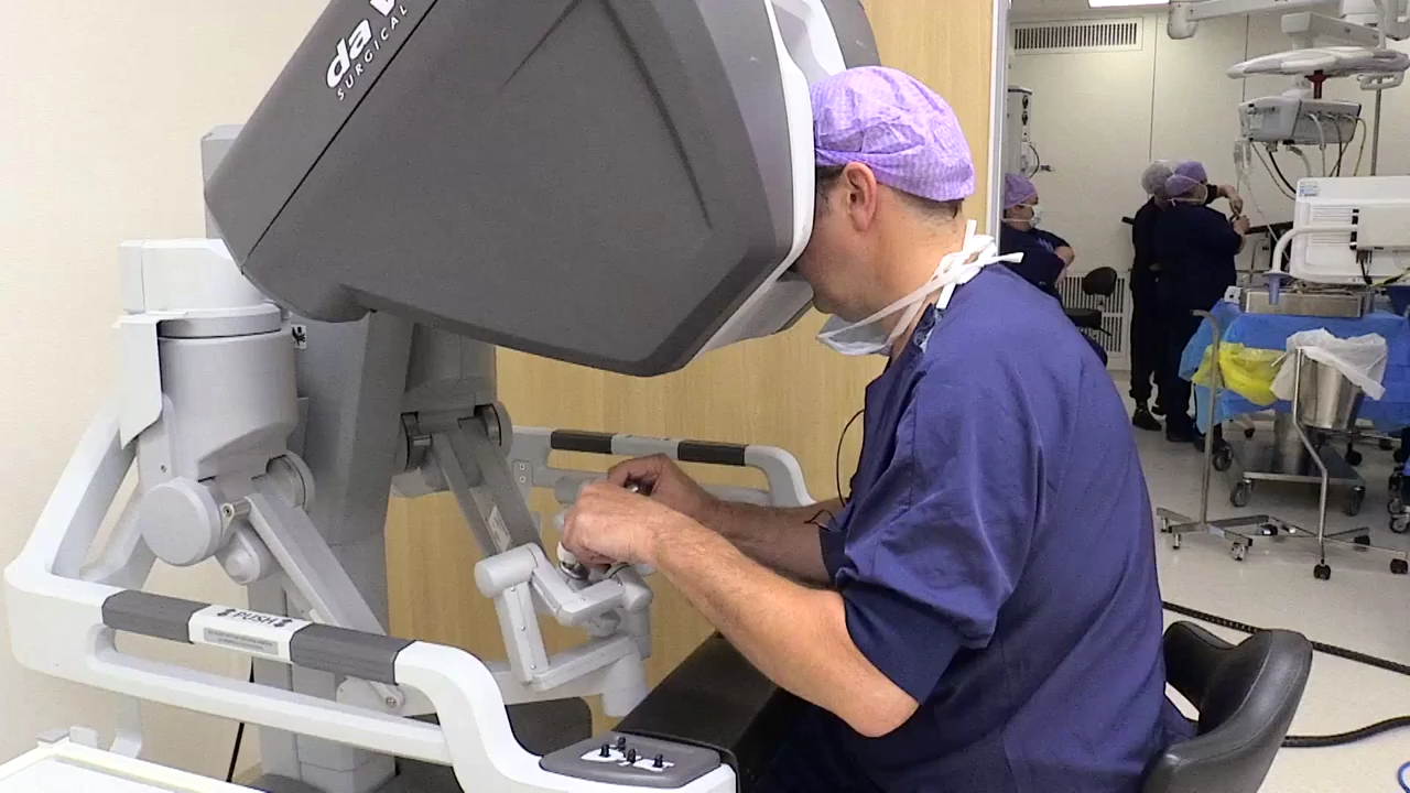 Persoon in OK-kleding bedient een operatierobot met handbediening in een robot-prostaatkankercentrum.