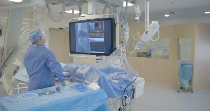 Zorgprofessional in scrubs en mondmasker bedient apparatuur en monitort gegevens op scherm in Catharina Ziekenhuis, met medische hulpmiddelen.