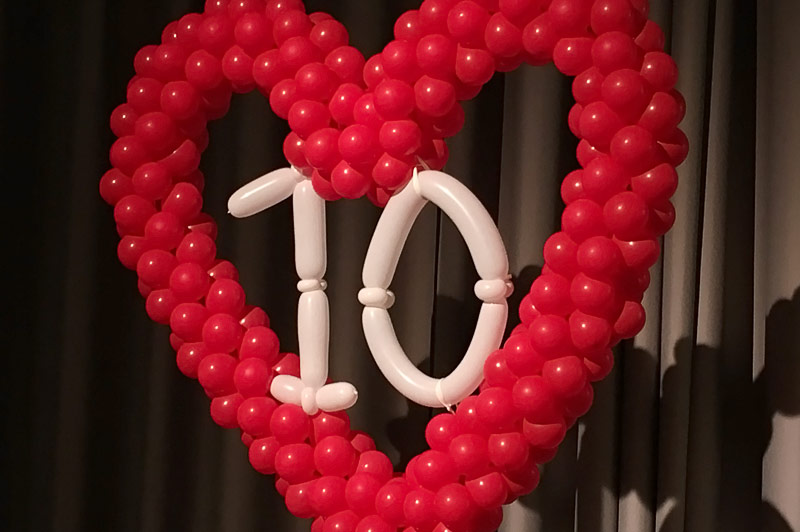 Grote hartvorm van rode ballonnen met '10' van witte ballonnen, voor gordijnen bij Hartweek in Catharina Ziekenhuis.