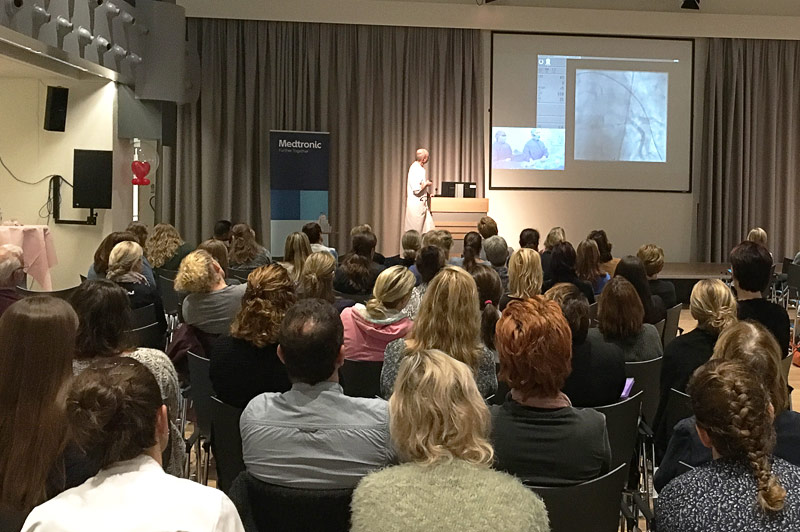 Spreker presenteert medische beelden tijdens Hartweek in zaal. Links grijze gordijnen en bord met Medtronic en Catharina Ziekenhuis.