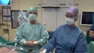 Twee medisch specialisten met mondmaskers en schorten staan in een operatiekamer met apparatuur, werkend aan buikvlieskanker.