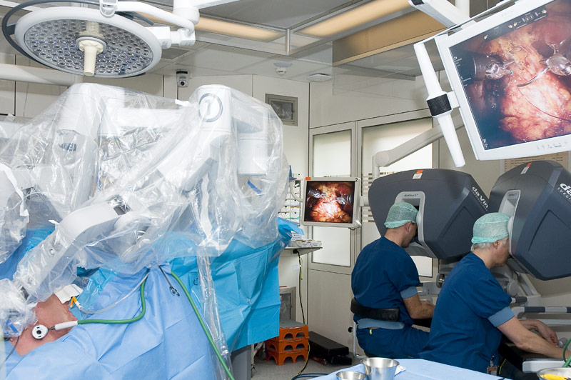 Twee chirurgen voeren robotchirurgie uit op een patiënt; instrumenten en monitors met intern beeld zijn zichtbaar.