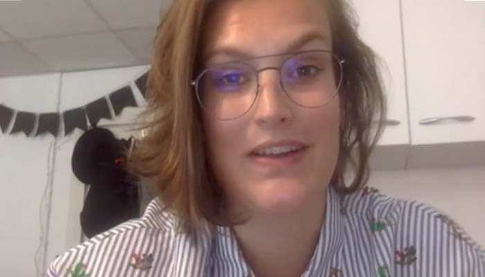 Persoon met halflang bruin haar en bril draagt een gestreept shirt. Op de achtergrond witte kasten en een slinger.