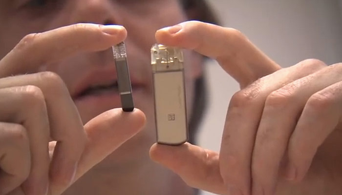 Iemand houdt een JUUL vape in de ene hand en een groter rechthoekig apparaat, vergelijkbaar met een mini-hartmonitor, in de andere.