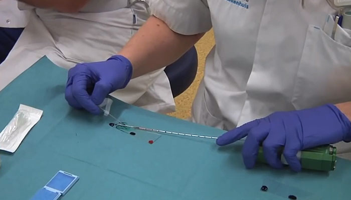 Persoon met paarse handschoenen en wit uniform bereidt medisch instrumentarium voor op een blauwe steriele doek.