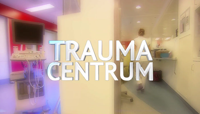 Ziekenhuisgang met kunst in witte jas, medische apparatuur links. Titel TRAUMA CENTRUM groot in beeld, Catharina Ziekenhuis.