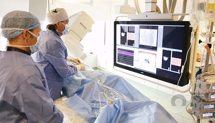 Twee medici in OK-kleding opereren in het Catharina Ziekenhuis en bekijken Philips medische beelden op een groot scherm.