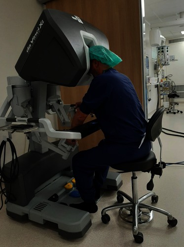 Een persoon in medische kleding en groene muts bedient een da Vinci operatieconsole tijdens een nieroperatie in een ziekenhuis.