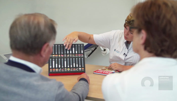 Een zorgverlener bespreekt met twee mensen een medicatie-overzicht aan een bureau, mogelijk i.v.m. nierziekten.