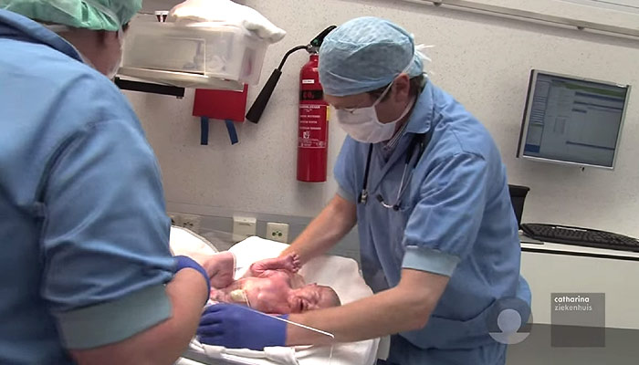 Twee zorgverleners in scrubs en maskers zorgen voor een pasgeborene op een ziekenhuisbed in een gynaecologische kliniek.