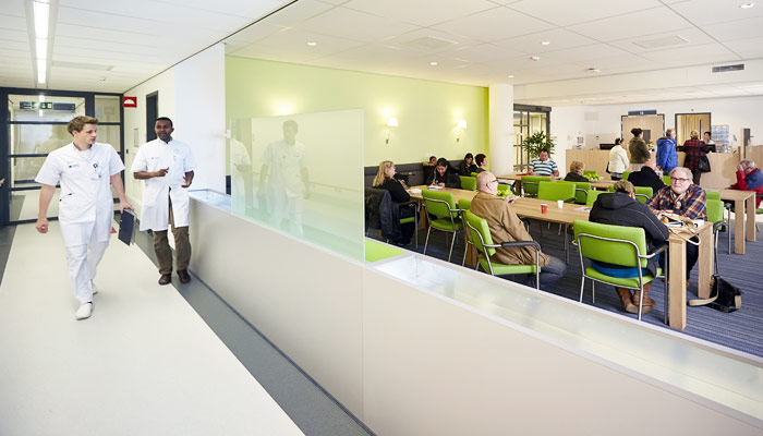 Moderne wachtruimte in het obesitascentrum met mensen op groene stoelen. Twee zorgverleners lopen door de gang.