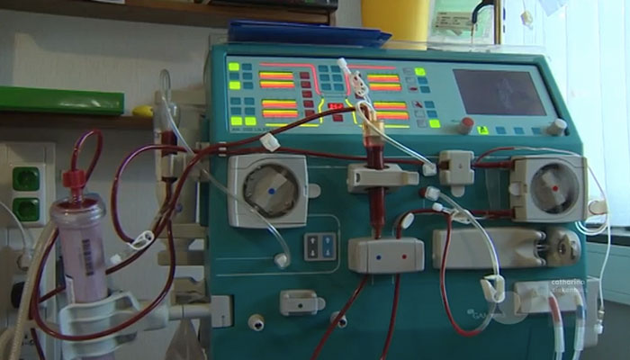 Dialyseapparaat met slangen en kabels, knoppen en schermen, in een medische kamer bij een raam voor voorlichtingsvideo.