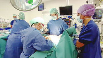 Chirurgen en medisch personeel in OK-kleding voeren een operatie uit in een fel verlichte operatiekamer.