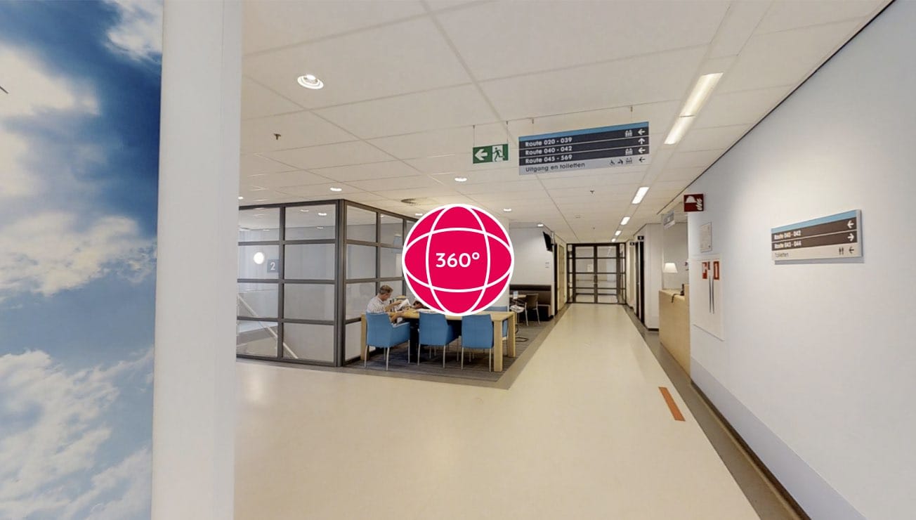 Lichte ziekenhuisgang bij Catharina Hart- en Vaatcentrum met witte muren, bewegwijzering en glazen zithoek met één persoon.