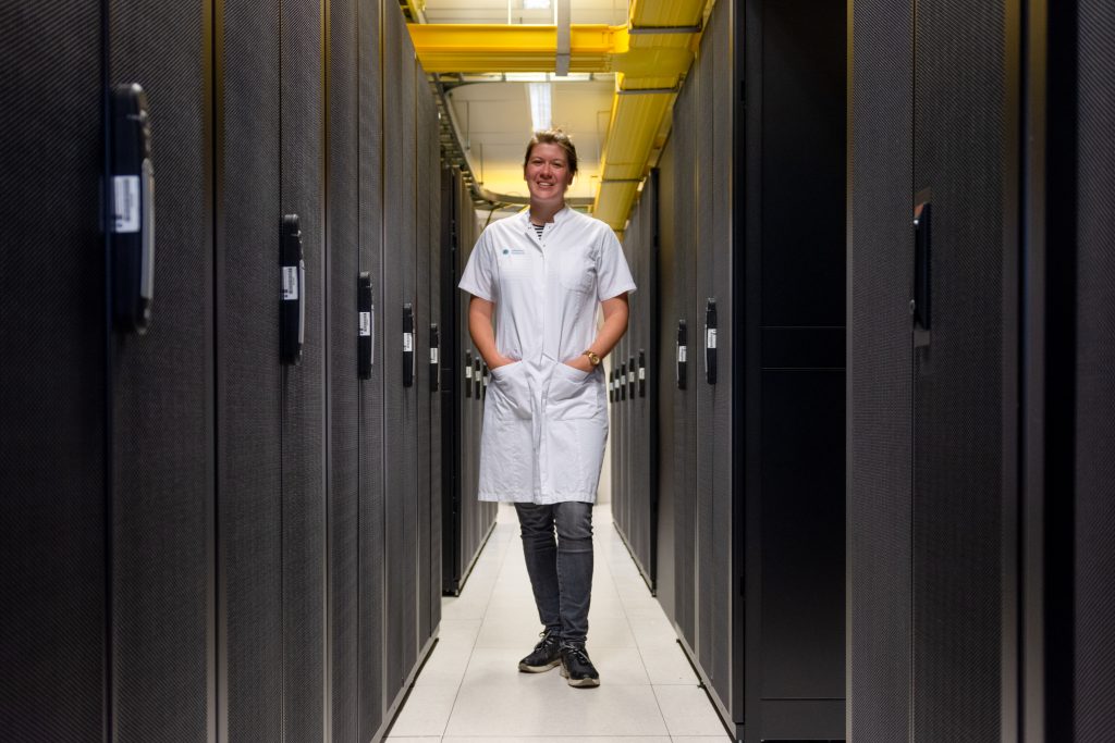 Persoon in witte labjas tussen serverrekken in verlichte datacenter onderzoekt gegevens voor vroege detectie van infarct of hartritmestoornis.