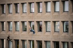 Twee personen dalen af langs de grijze gevel van het Catharina Ziekenhuis, terwijl mensen binnen toekijken.