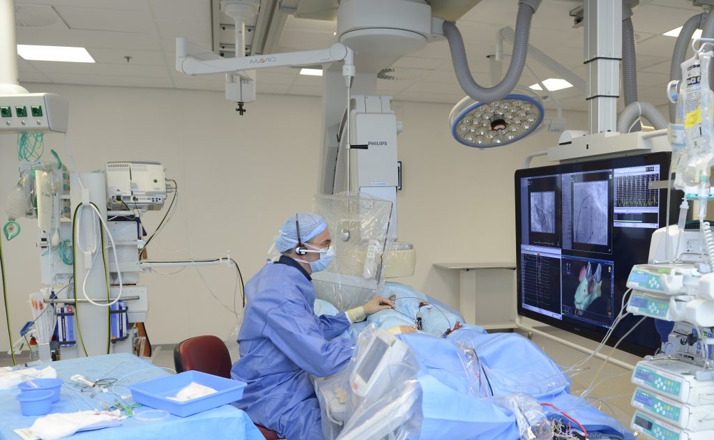Een arts in OK-kleding bedient apparatuur terwijl cardiologen monitoren bekijken bij een ablatie voor hartritmestoornissen.