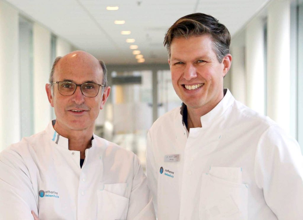 Twee mannen in witte jassen staan naast elkaar in een heldere gang van het beste ziekenhuis, kijkend naar de camera.