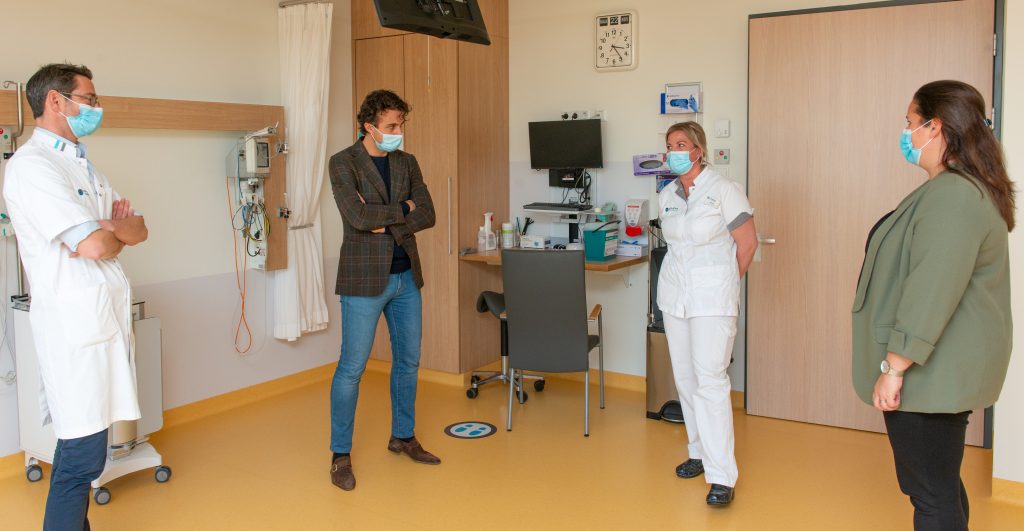 Vier volwassenen, waarvan twee in witte medische uniformen en allen met mondkapje, staan op afstand in een kamer van het Catharina Ziekenhuis.