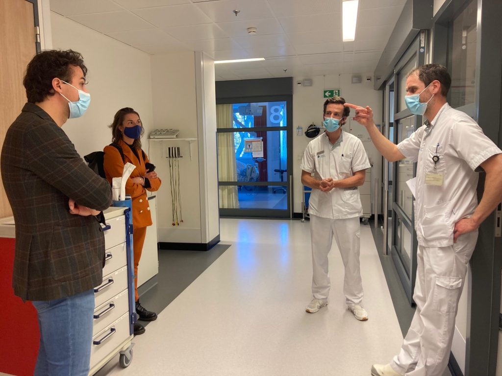 Vier mensen in een ziekenhuisgang bij Catharina Ziekenhuis; twee artsen praten met twee bezoekers, medische apparatuur naast hen.